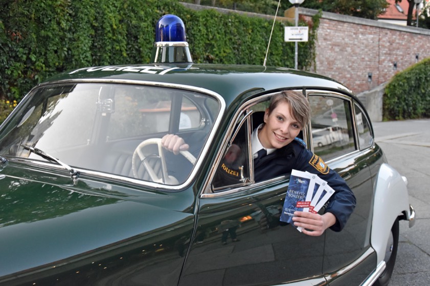 Eine Polizistin rührt im Polizei-Oldtimer die Werbetrommel für das Benefiz-Konzert in Ingolstadt. Foto: Polizei