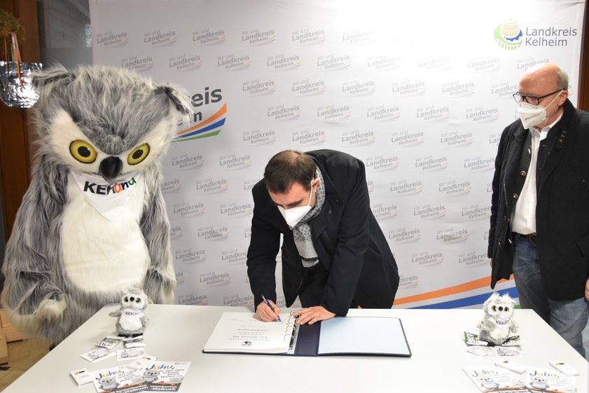 Neben dem Maskottchen "KEHUhu" stehend, trug sich der bayerische Gesundheits-Minister Klaus Holetschek heute im Rahmen seines Besuchs in Kelheim ins Gästebuch des Landkreises ein. Rechts Landrat Martin Neumeyer. Foto: Lukas Sendtner, Landratsamt Kelheim