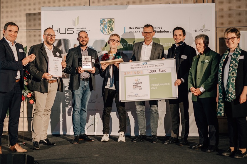 Landrat Albert Gürtner (links), Thomas Lange (Vierter von rechts; Vorstands-Mitglied der Volksbank-Raiffeisenbank Bayern-Mitte), KUS-Chef Johannes Hofner (Dritter von rechts), Bernd Huber (Zweiter von rechts; Ehrenvorsitzender des Wirtschafts-Beirats des Landkreises) und VHS-Chefin Alice Köstler-Hösl (rechts) überreichten den Preis "Wirtschaft macht Inklusion" an Geschäftsführer Maximilian Knoll (Zweiter von links), Prokurist Alexander Knoll (Dritter von links) und Mitarbeiter Jonas Fischl (Vierter von links). Fotos: KUS /anni's art